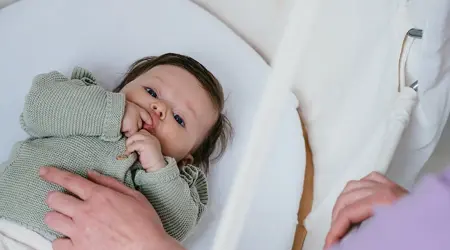 Baby ligt in craddle met vinger in mond