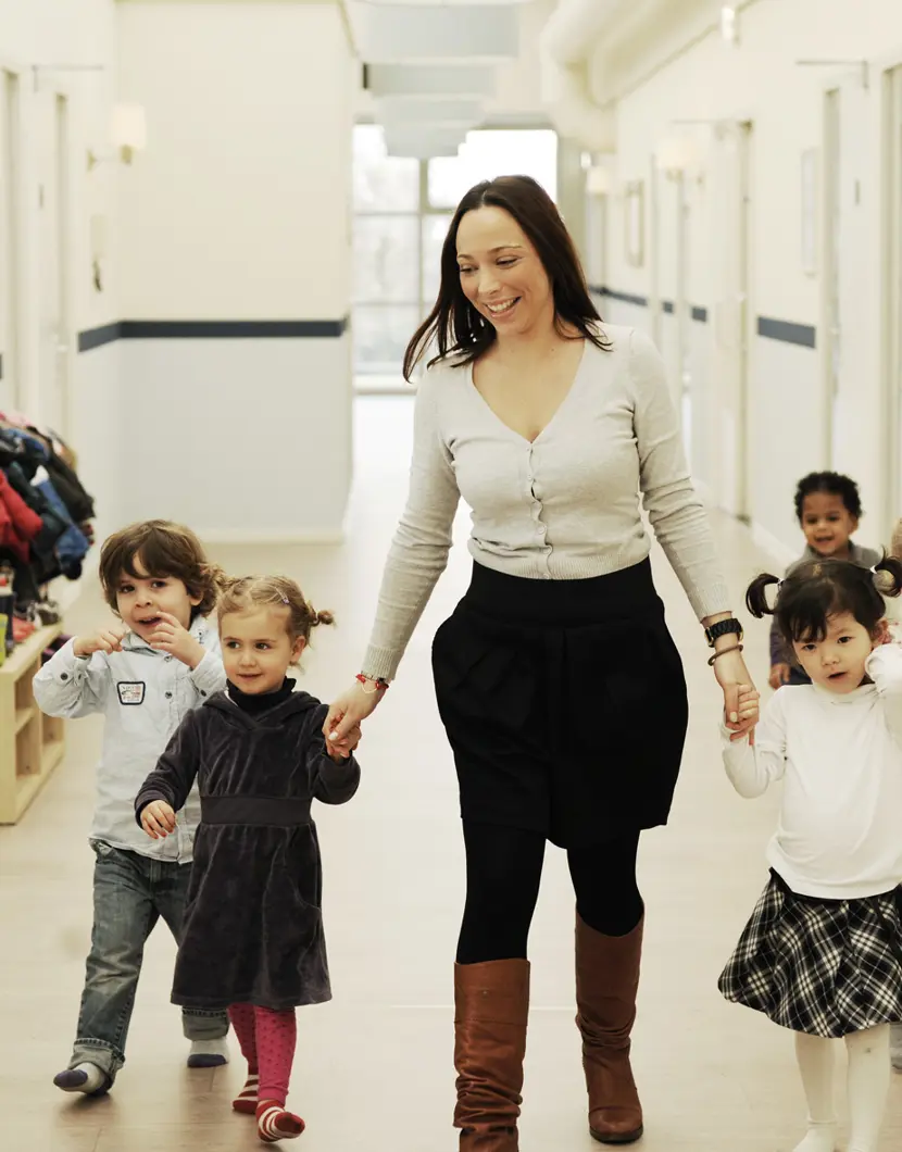 pedagogisch medewerker loopt met kinderen door gang kinderopvang