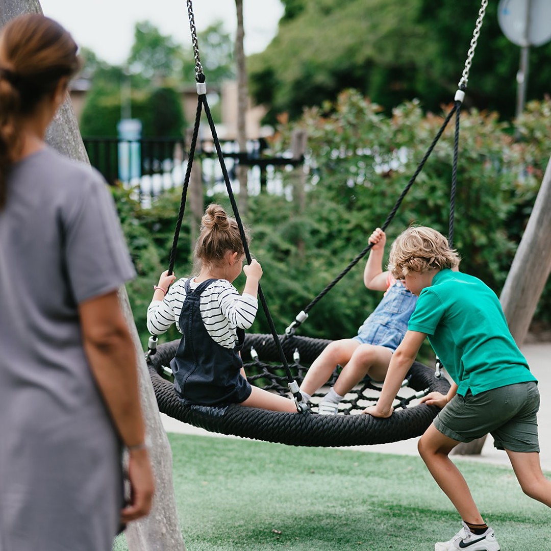 Kinderen spelen op schommel en vrouw kijkt toe