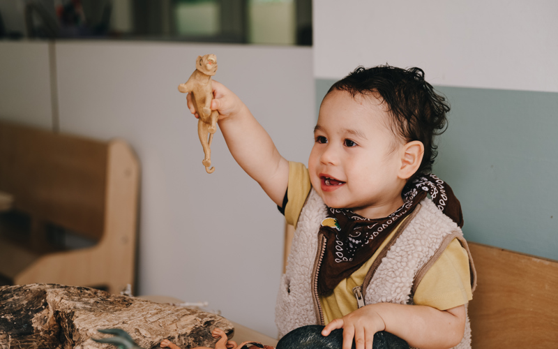 Kind houdt speelgoed dino omhoog en lacht