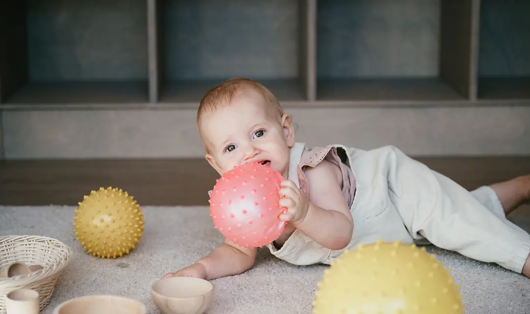 Baby ligt op de grond met bal in hand