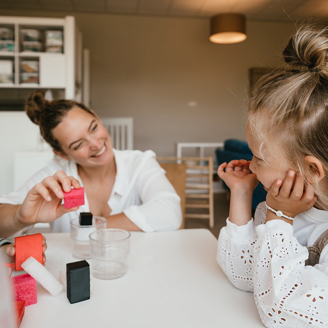 Pedagogisch Medewerker speelt en lacht met kinderen aan tafel