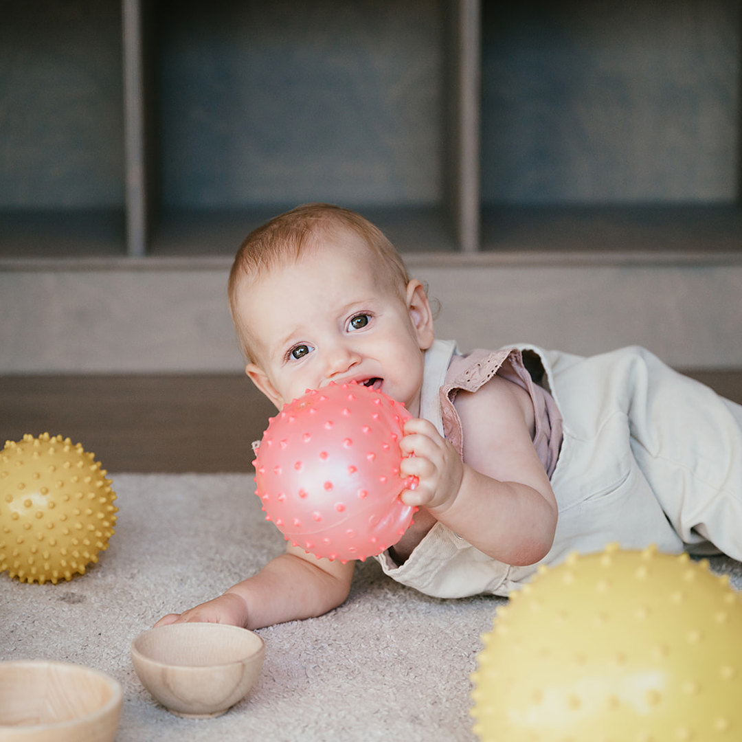 Baby ligt op de grond met bal in hand