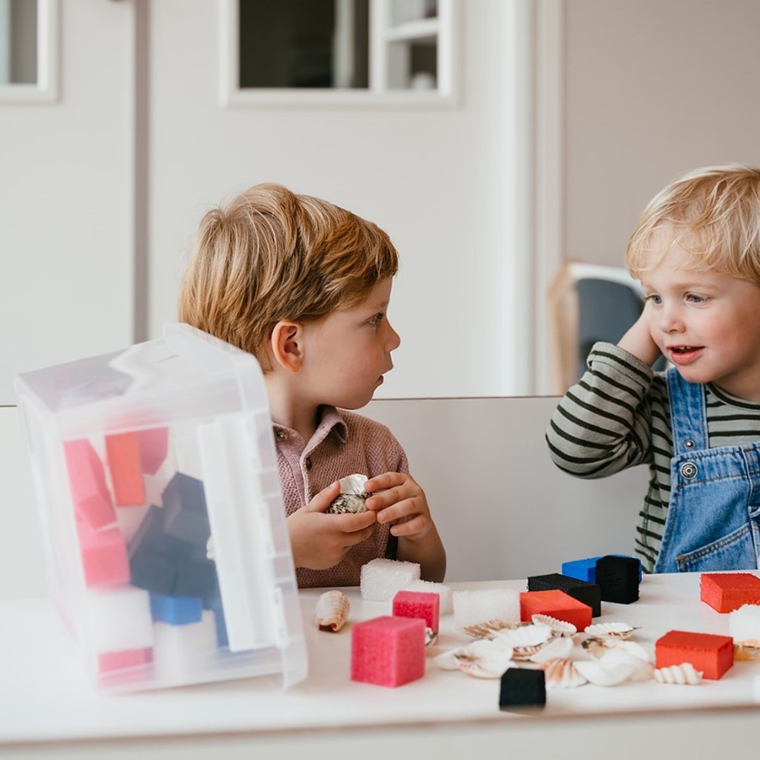 Twee peuters zitten aan tafel en spelen met passief speelgoed