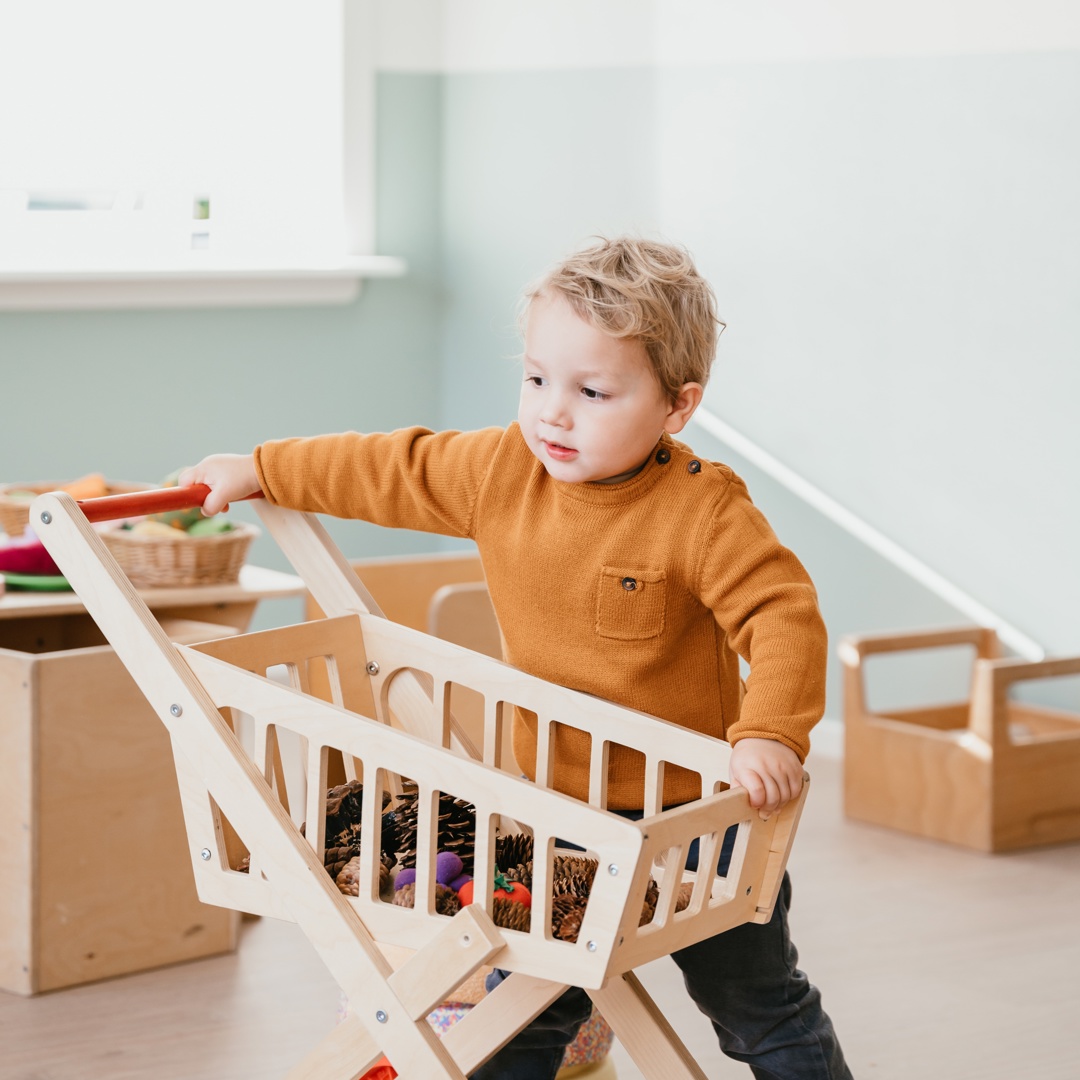Peuter speelt met houten winkelwagen
