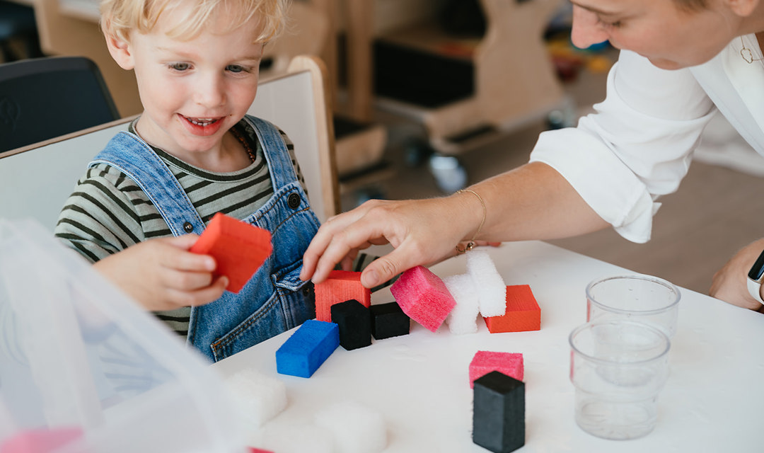 kind en pedagogisch medewerker spelen aan tafel