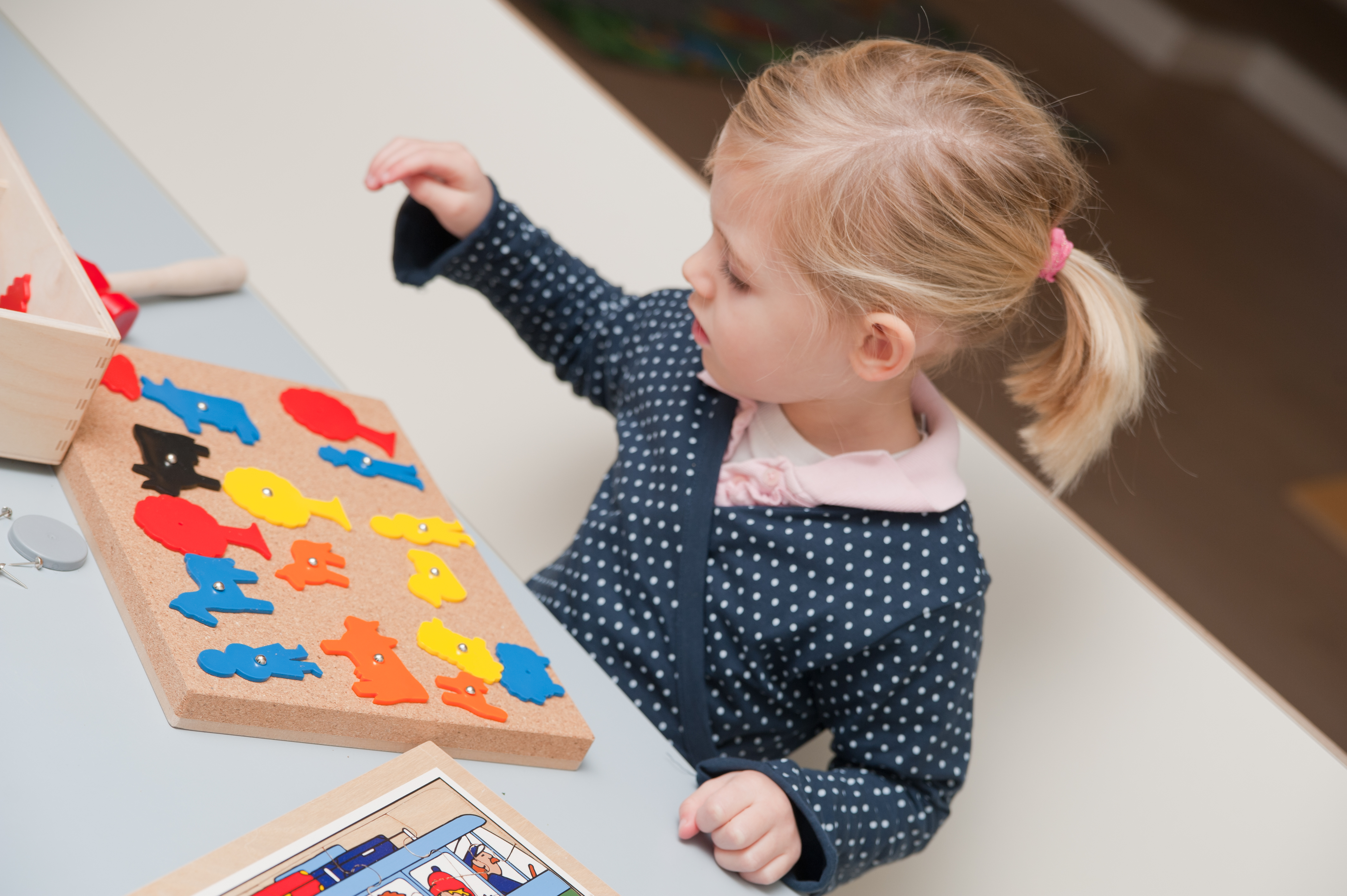 kind zit aan tafel en speelt met prikbord
