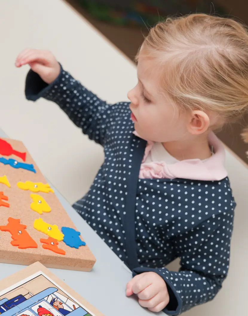 kind zit aan tafel en speelt met prikbord