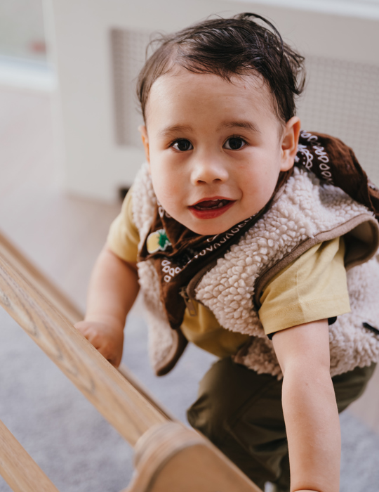 Kind klimt op een klimdriehoek en kijkt in camera