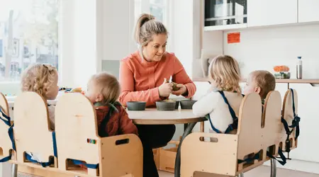 Pedagogisch Medewerker op kinderopvang snijdt fruit voor kinderen aan tafel