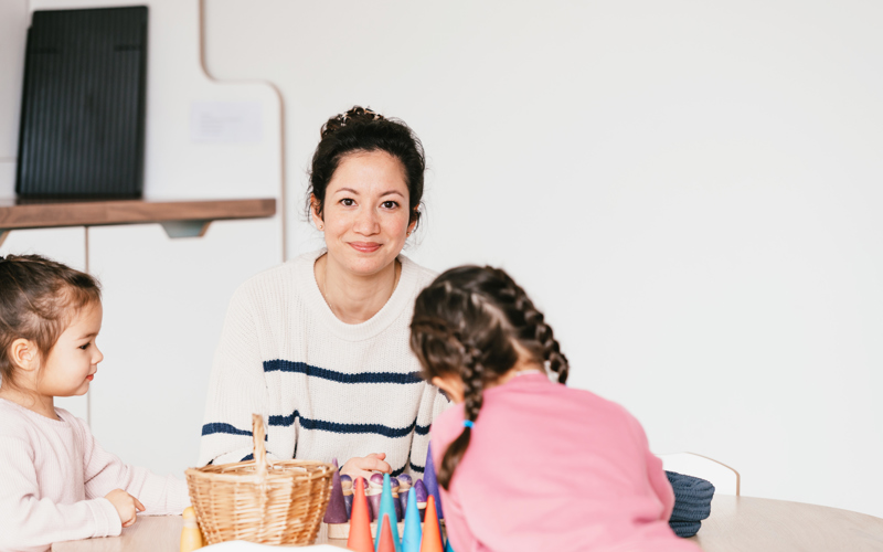Vrouw zit aan tafel met kinderen en kijkt in de camera