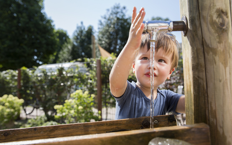 Peuter speel met water bij kraan in tuin