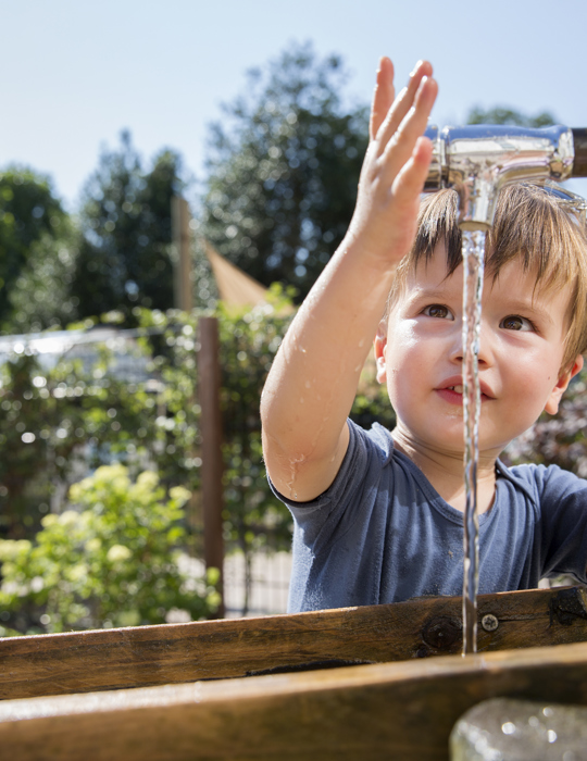 Peuter speel met water bij kraan in tuin