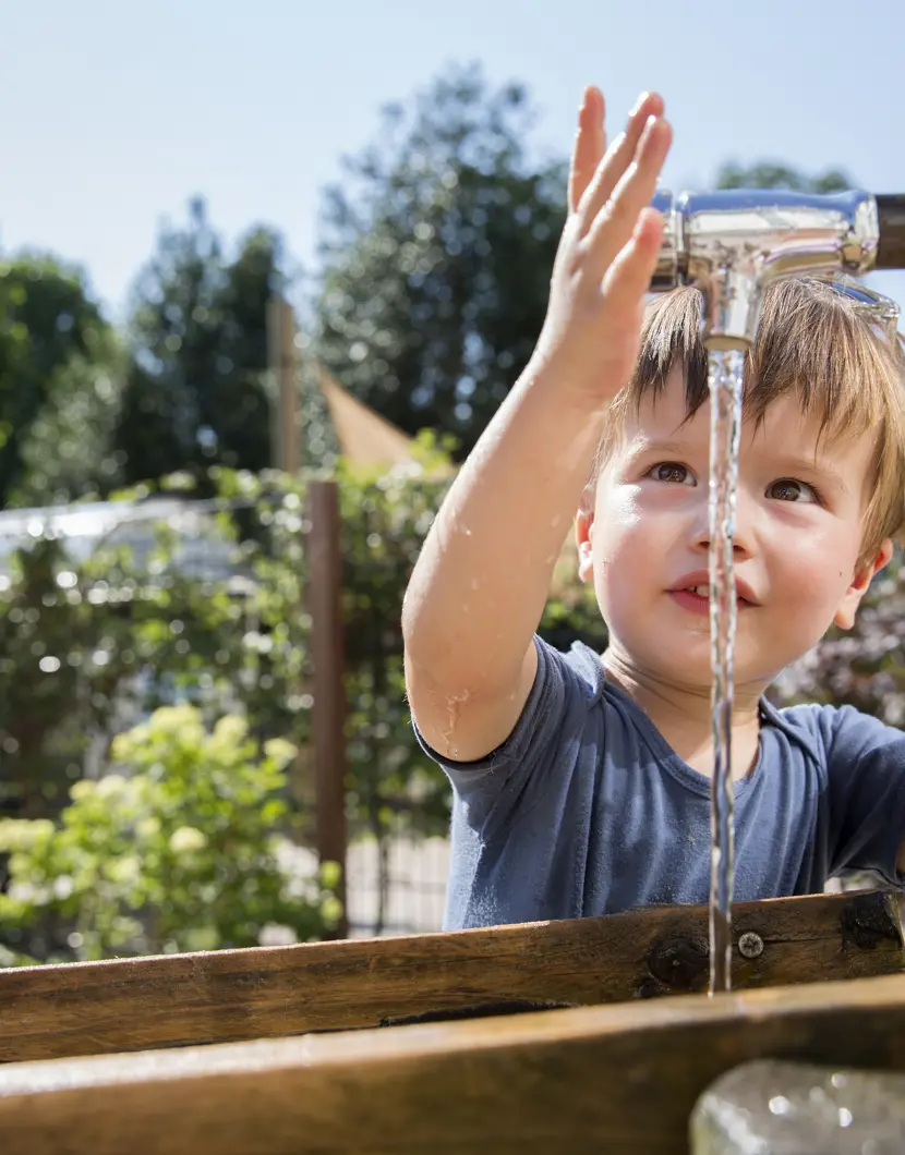 Peuter speel met water bij kraan in tuin