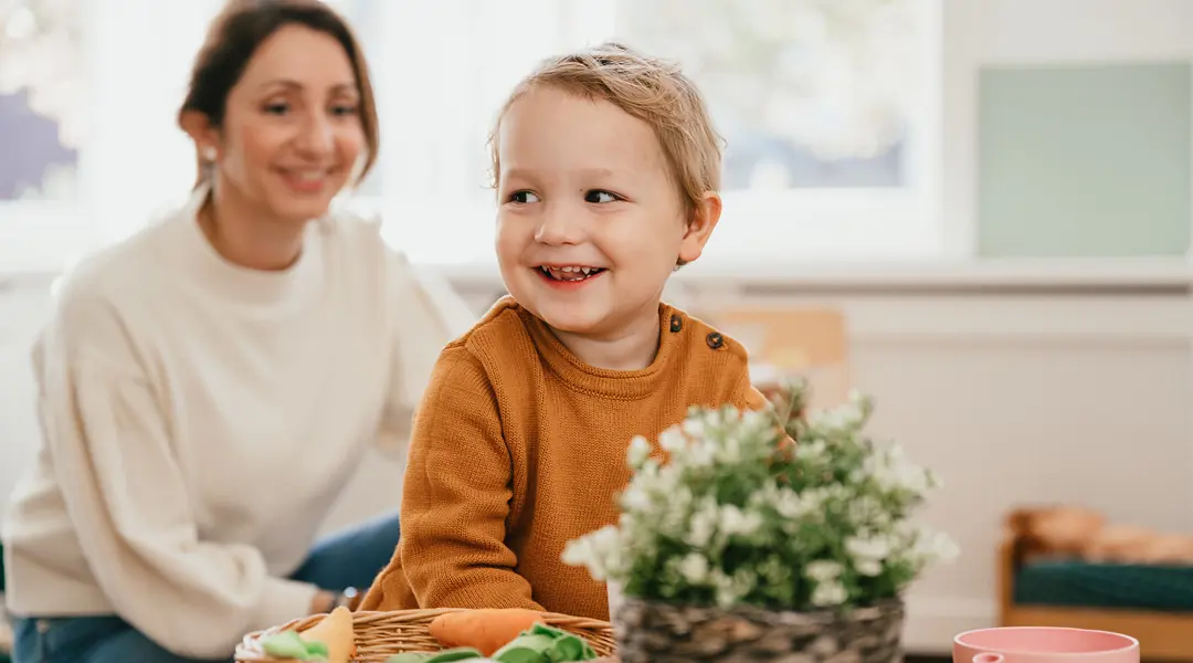 Dreumes speelt aan tafel met speelgoed en vrouw helpt
