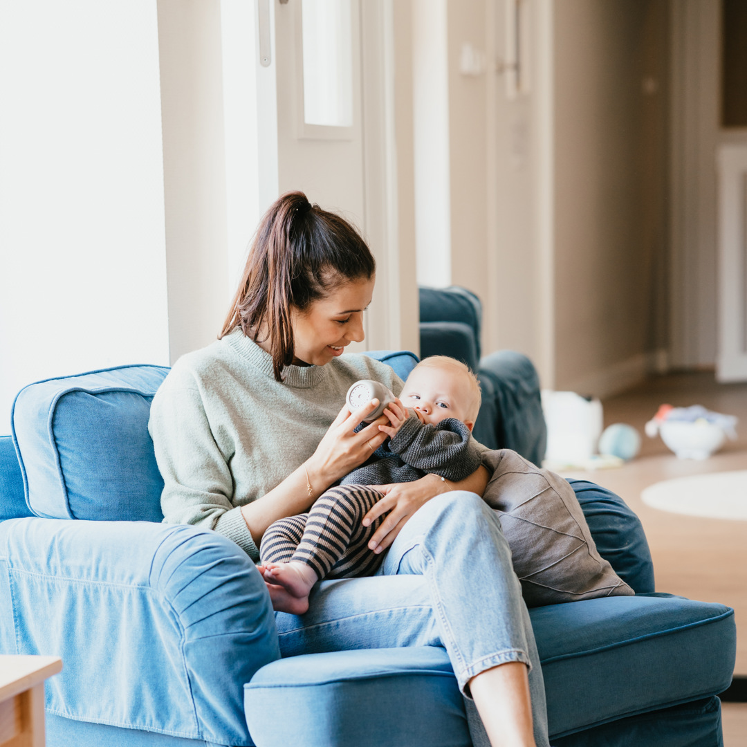 Zwangere vrouw geeft baby een fles op schoot