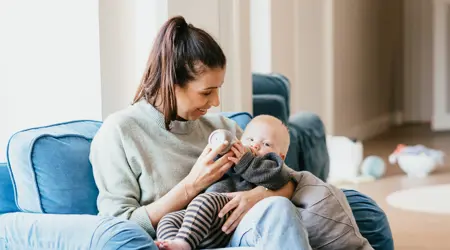 Zwangere vrouw geeft baby een fles op schoot