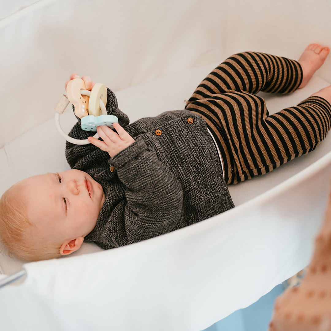 Baby ligt met speelgoed in craddle