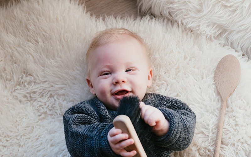 Baby ligt lachend op de grond met speelgoed in handen