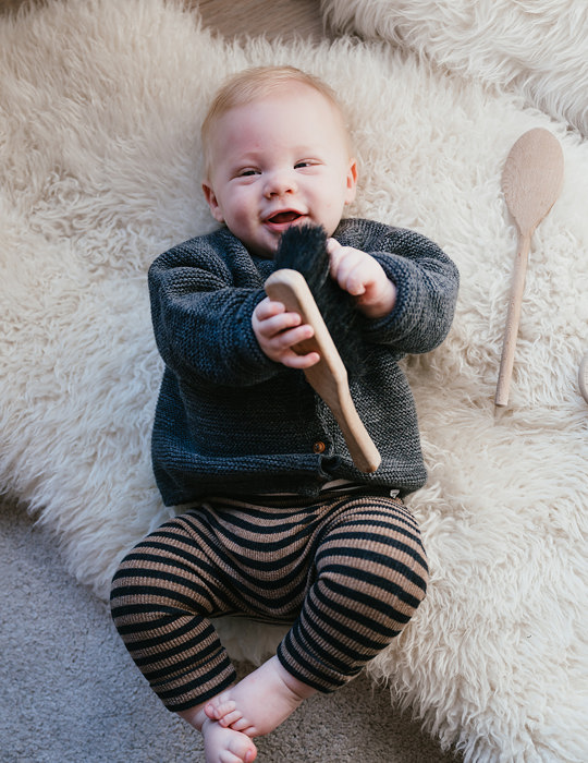 Baby ligt lachend op de grond met speelgoed in handen