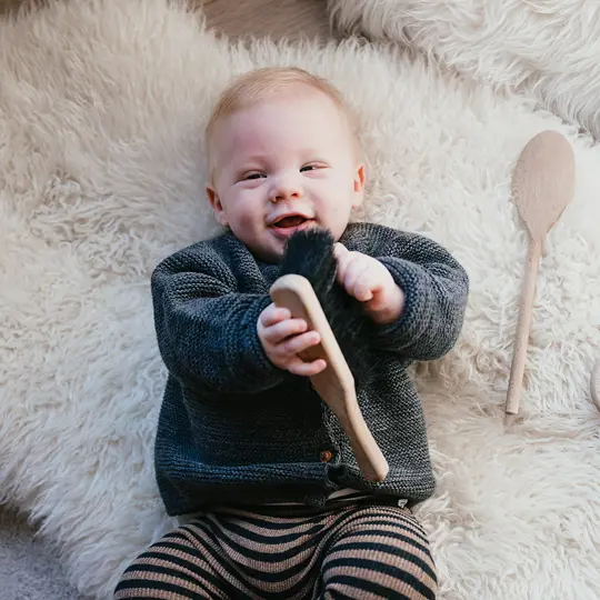 Baby ligt lachend op de grond met speelgoed in handen