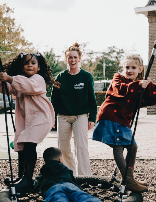 Kinderen op een schommel en een vrouw op de achtergrond die blij toekijkt