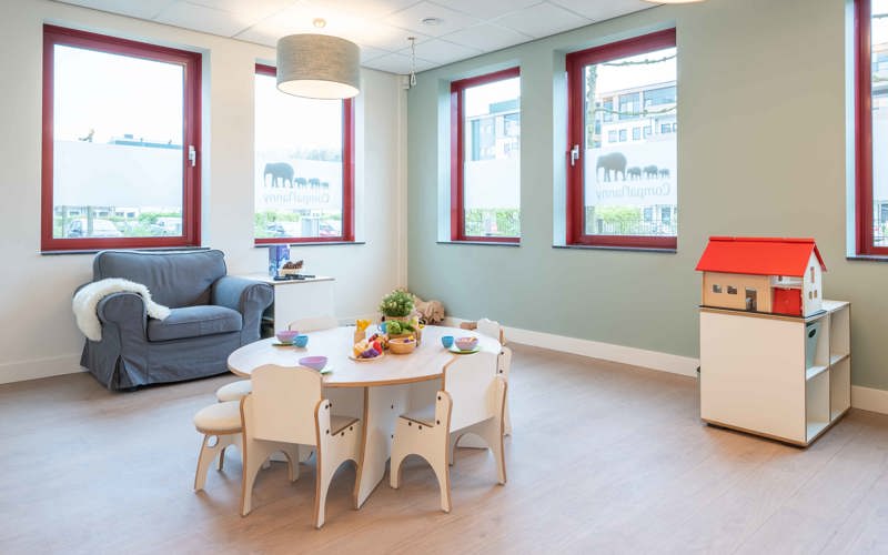 groep kinderopvang met kleine tafel en stoelen en een grote lounge stoel