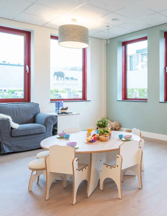 groep kinderopvang met kleine tafel en stoelen en een grote lounge stoel