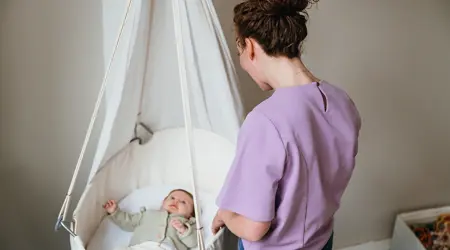 Baby ligt in craddle vrouw staat ernaast