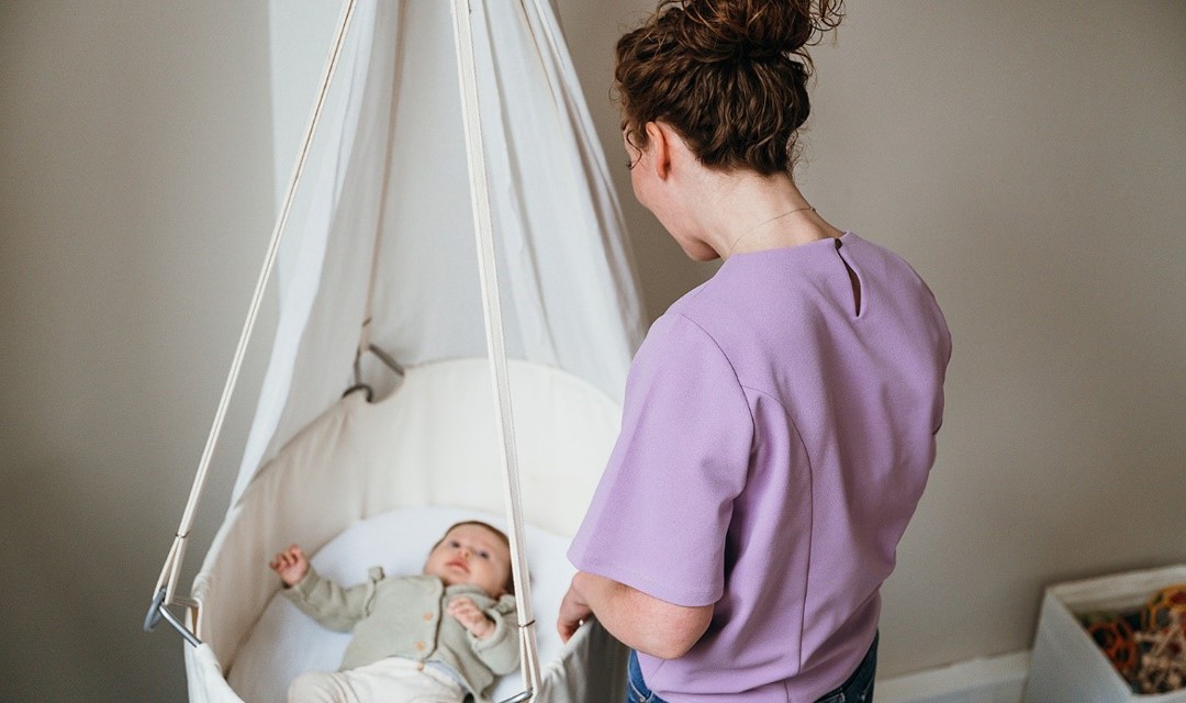 Baby ligt in craddle vrouw staat ernaast